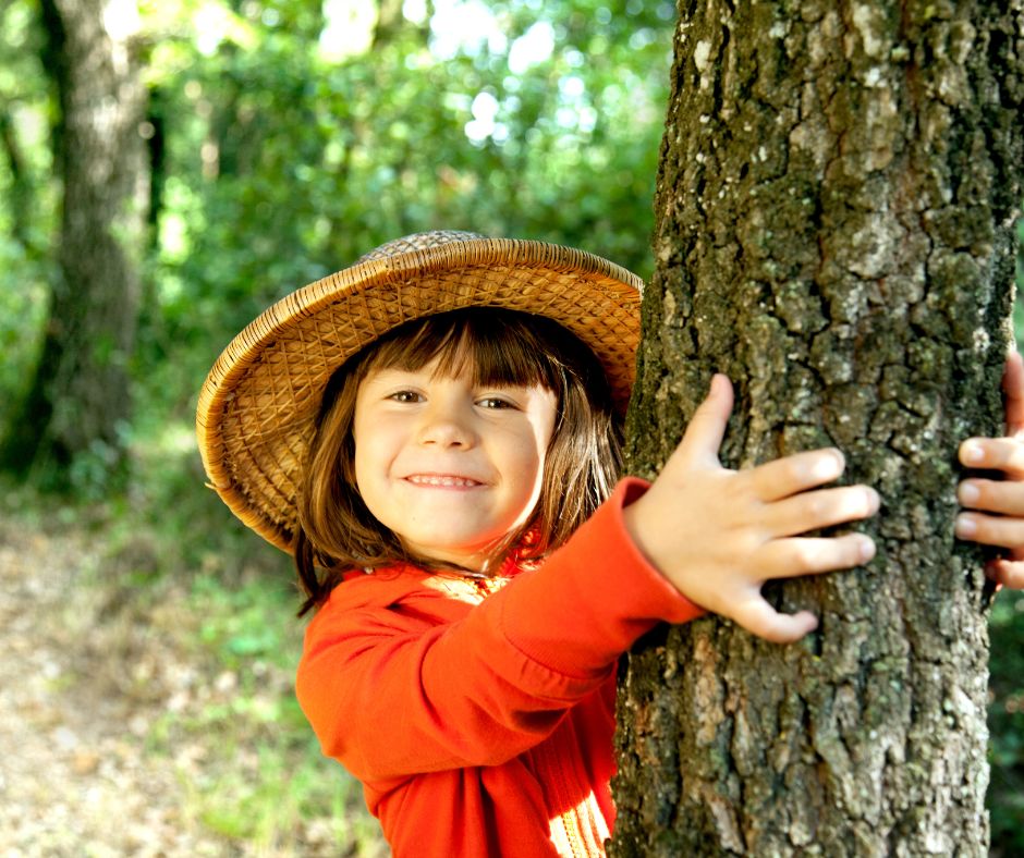 Kind mit Hut umarmt einen Baum.